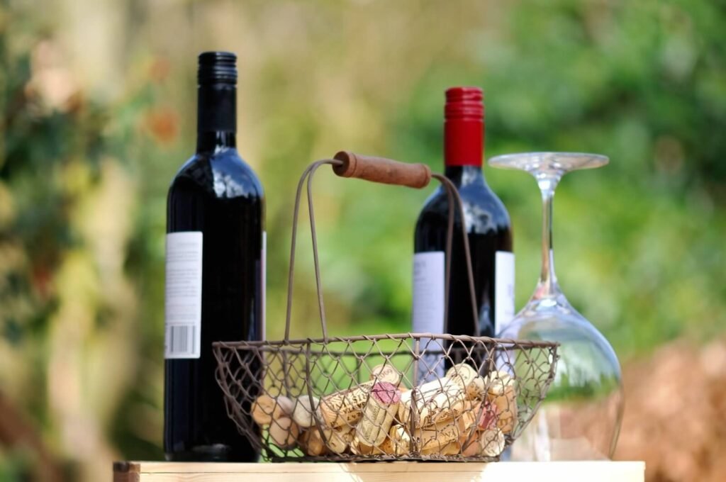 Botellas de vino tinto, cesta de corchos y copa vacía invertida sobre barril de madera